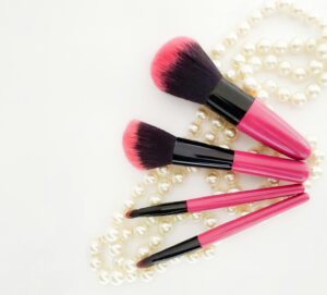 Pink and black makeup brushes arranged on pearl necklace for elegant look.