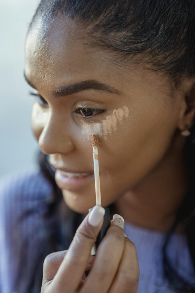 Close-up of a young woman applying concealer, highlighting her skincare routine for a flawless complexion.