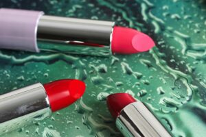 Close-up of three colorful lipsticks on a textured green surface, showcasing modern cosmetics.